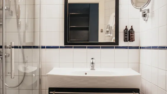 A clean and modern bathroom at Home Hotel Kung Oscar with a white sink, mirror, and a shower area. The floor has a checkered pattern.