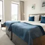 Et lyst hotellrom med to senger, blå detaljer, et skrivebord ved vinduet og kunst på veggen, for et komfortabelt opphold.