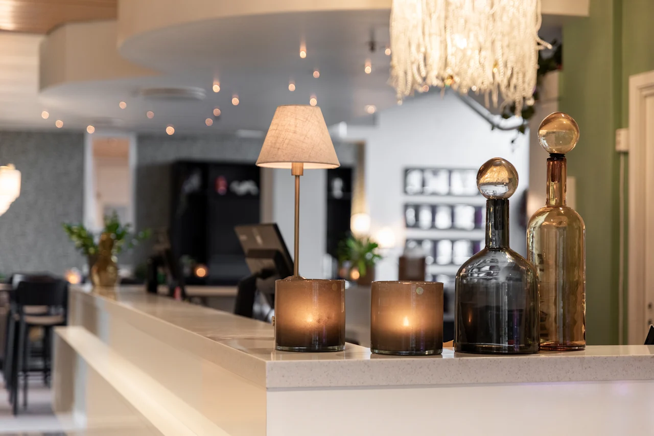 Lämmin ja kutsuva hotelliaula tai baarialue, jossa on koristevalaistusta, kynttilöitä ja pulloja tiskillä.