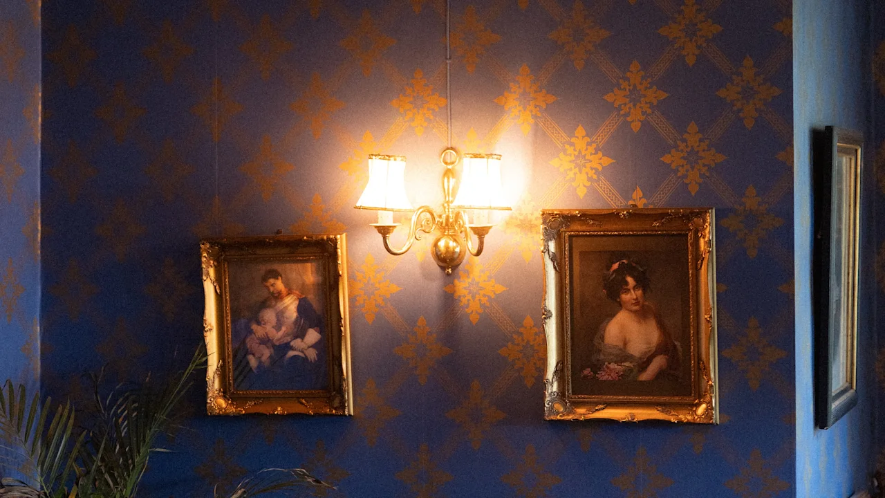 In an elegant corner of Dalen Hotel, a soft light illuminates classic paintings on blue patterned walls. A vintage clock and warm decor create a nostalgic ambiance.