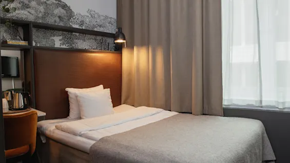 Et indbydende hotelværelse med en enkeltseng, varm belysning og et funktionelt arbejdsområde, perfekt til et behageligt ophold.