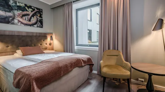 Et koselig hotellrom med en komfortabel seng, en stilig lenestol og et lite bord, perfekt for avslapning eller en rask lesestund.