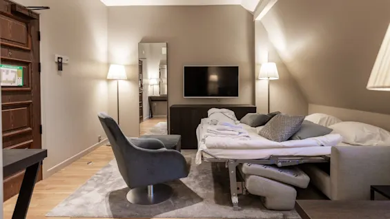 A pull-out sofa bed is extended, covered with pillows and a blanket, facing a TV on a cabinet. Two floor lamps illuminate the modern living space.