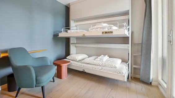 A wall-mounted Murphy bunk bed is partially extended in a modern room with a blue-green wall, wooden floor, and minimalist furniture.