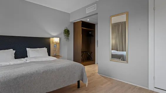 Ett mysigt hotellrum med en bekväm säng, en sänglampa och en spegel som reflekterar rummets inbjudande atmosfär.