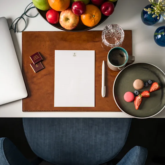 A neatly arranged desk with a laptop, fresh fruit, coffee, and a sweet treat, suggesting a productive and enjoyable workspace.