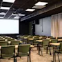 A modern conference room with rows of tables and chairs facing a large projection screen, ready for a presentation.