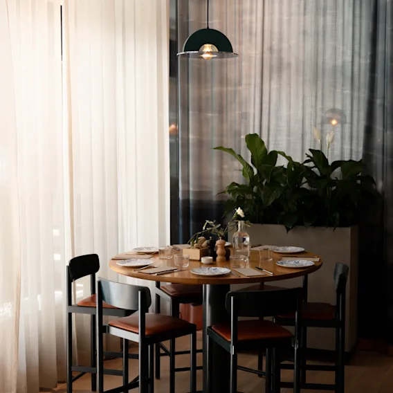Ett mysigt runt matbord i trä dukat för en måltid med höga stolar och en hängande lampa i en modern restaurang.