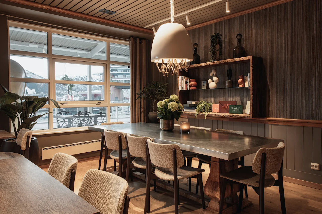An elegant dining or meeting room featuring a long wooden table, comfortable chairs, and a large window overlooking a scenic view.