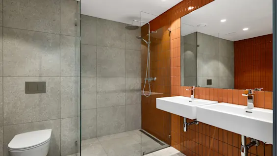 Et moderne bad med dusj, toalett og dobbel servant, med grå og oransje flislagte vegger.