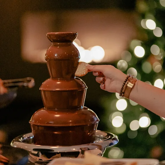 Dippe en kjeks i en rennende sjokoladefontene med et juletre i bakgrunnen