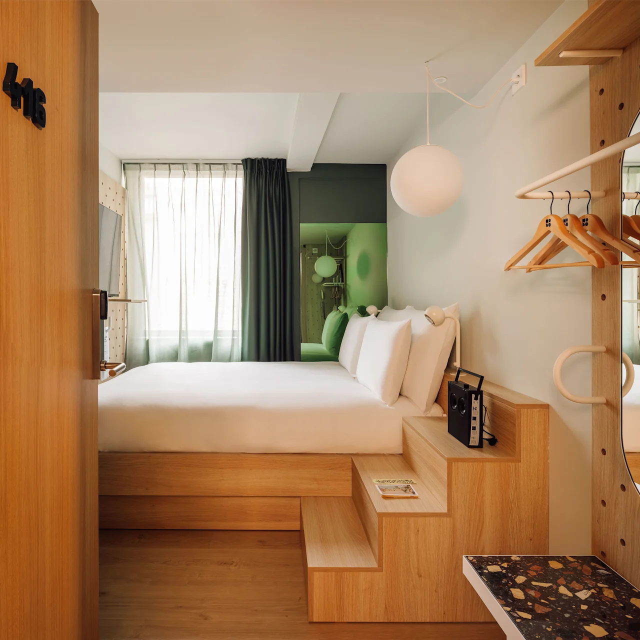 Hobo Oslo hotel room, featuring a minimalist design with a raised bed, wooden storage, and a bright window.