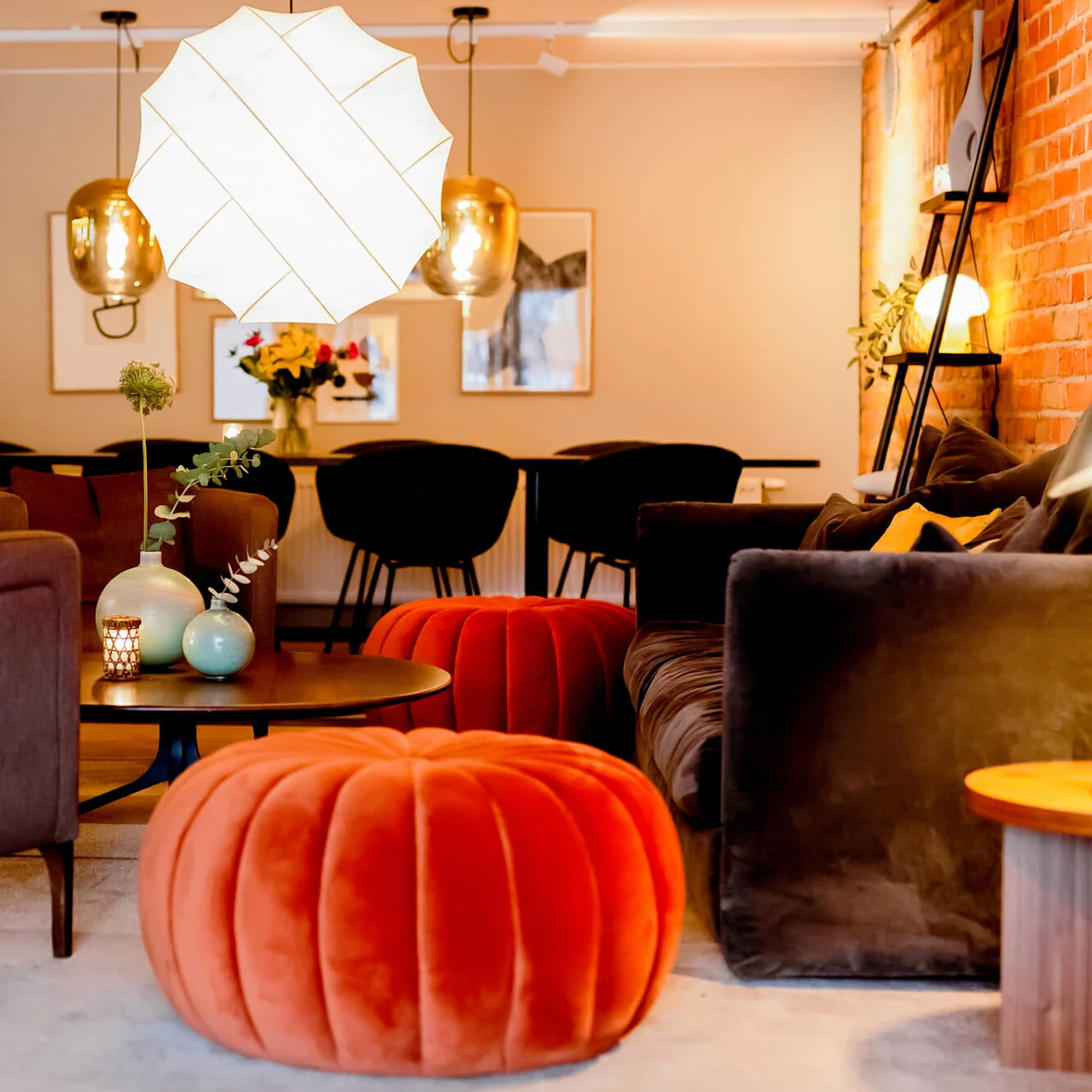 Cozy lounge area with modern sofas, armchairs, and decorative lighting, in a warm setting with brick and painted walls.