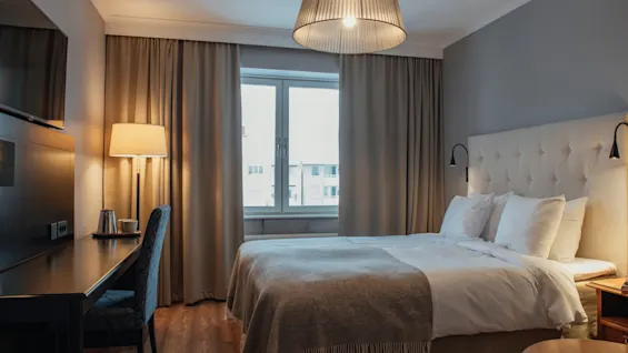 Ett mysigt hotellrum med en bekväm säng, en skrivbordsplats och ett fönster med naturligt ljus.