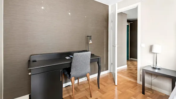 A modern minimalist office room with a black desk, grey chair, and decorative wall lamps; parquet flooring adds warmth.