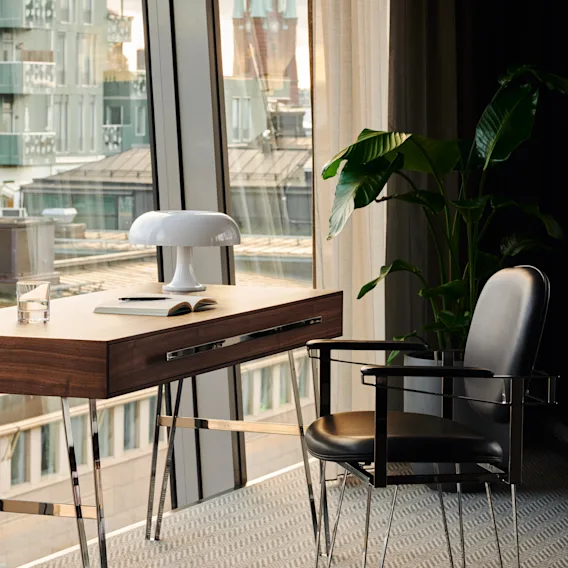 En stilren arbetsplats med skrivbord, stol och lampa, med utsikt över staden. Stratum Suite av Bernadotte och Kylberg på Clarion Hotel Sign i Stockholm.