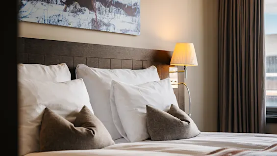 Mysigt hotellrum med en bäddad säng, mjuka kuddar och en tänd sänglampa som sprider ett varmt sken.