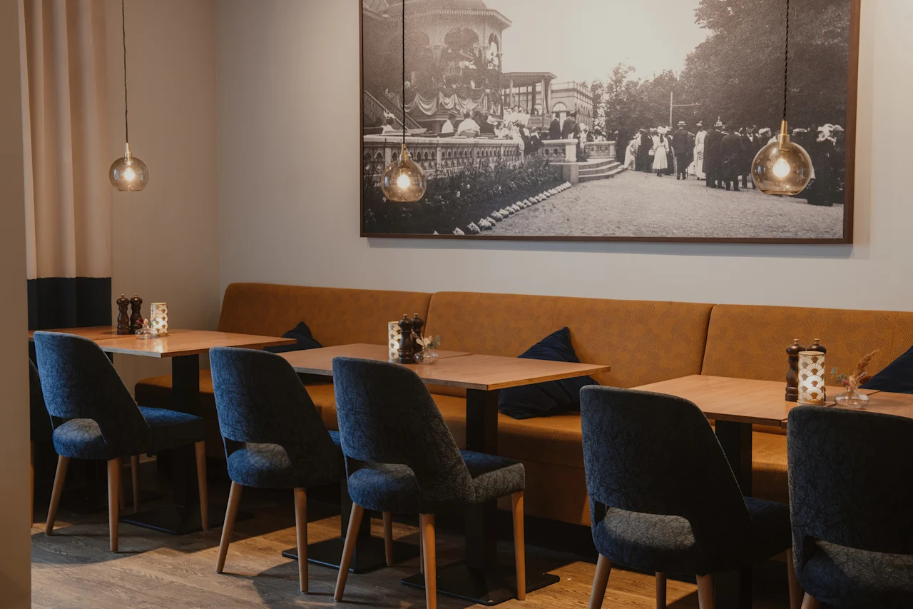 Et komfortabelt restaurantområde med træborde, mørke stole og en lang brun bås, under et stort vægbillede.