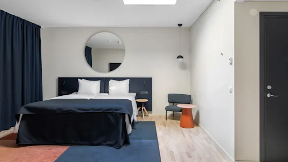 Et moderne hotelværelse med en komfortabel seng, et rundt spejl og stilfulde møbler, der tilbyder et afslappende ophold.
