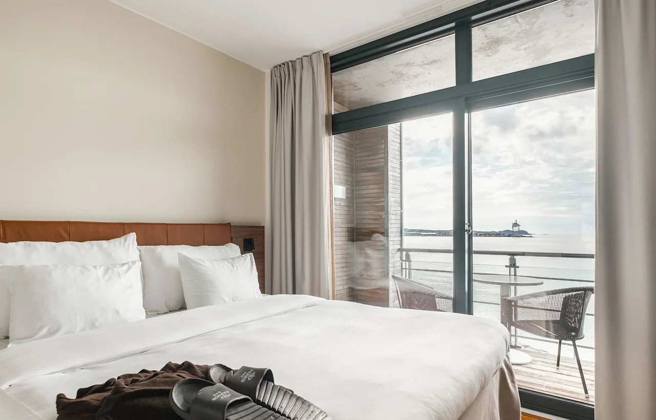 A comfortable hotel room at Farris Bad in Larvik with a bed, slippers, and a robe, featuring a balcony overlooking the sea.