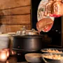 Et rustikt buffetbord med en suppevarmer, stablede tallerkener og madskåle, oplyst af varm belysning. KARET TIL SANDESJORD.