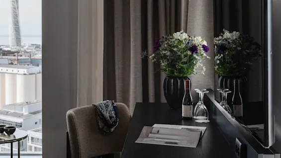 Et moderne hotellrom med skrivebord, blomster og byutsikt med en karakteristisk høy bygning.