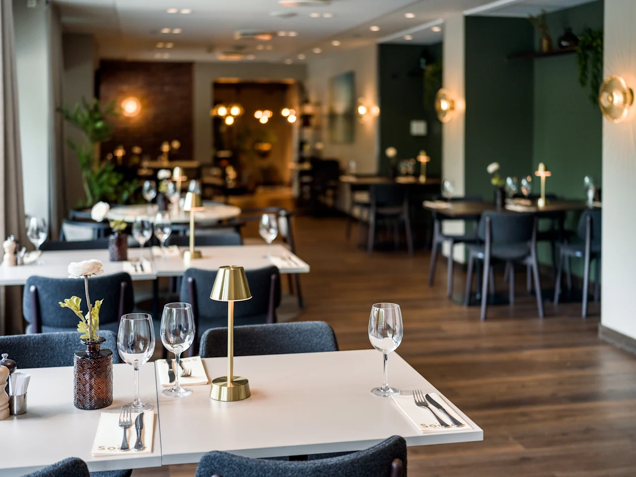 Vackert dukade matbord med vinglas och små lampor i en elegant restaurang, med stämningsbelysning och mörk, modern inredning som skapar en varm och inbjudande atmosfär.