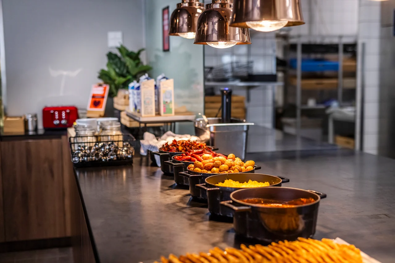 A warm and inviting breakfast buffet at Comfort Hotel Vesterbro, offering a variety of hot dishes under stylish pendant lights.