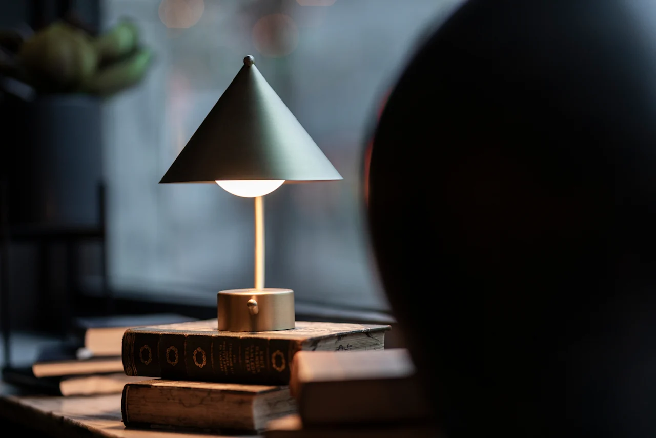 A warm, inviting lamp illuminates a stack of old books, creating a cozy atmosphere at Home Hotel Grand Bodø.