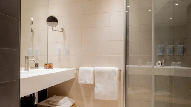 A modern bathroom with a walk-in shower and floating vanity against tiled walls, illuminated by ceiling lights.