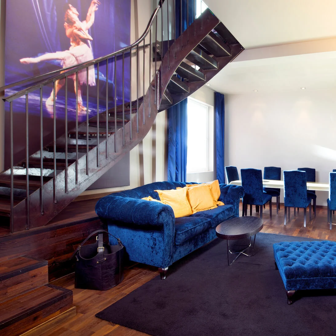 En stilig stue med blå fløyelsmøbler og en spiraltrapp som fører oppover; moderne chic interiørdesign.