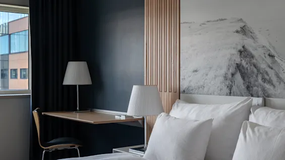 A cozy and modern hotel room at Clarion Hotel Sign with a comfortable bed, a desk area, and a mountain-themed wall art.