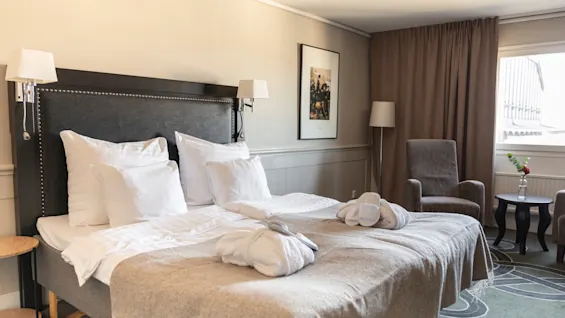 Ett bekvämt hotellrum på Home Hotel Tapto i Stockholm, med en prydligt bäddad säng, badrockar och tofflor, inbjudande till avkoppling.