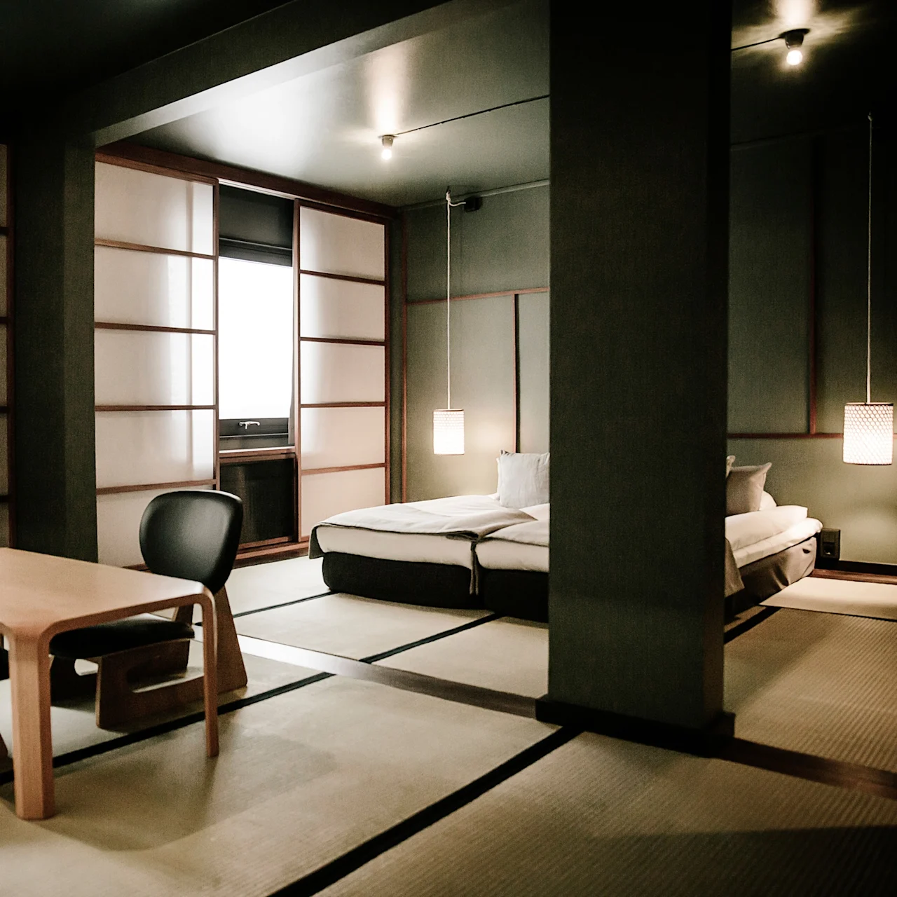 Et minimalistisk japansk stil rom med tatamigulv, et lavt bord med stoler og en seng, viser tradisjonelle og moderne elementer.