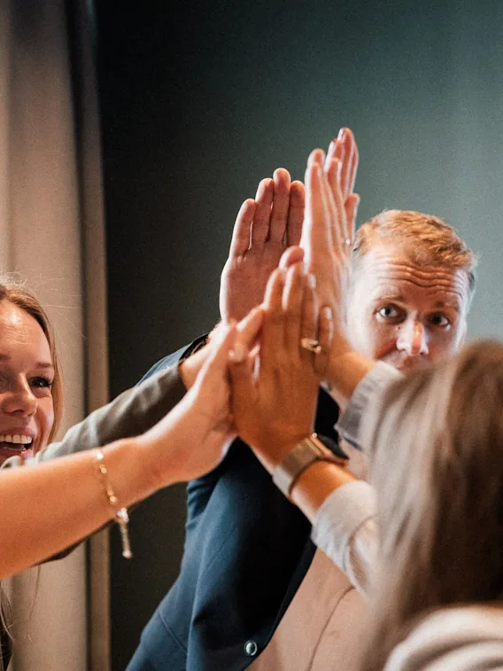 En gruppe smilende kollegaer som feirer godt samarbeid med en high-five under et møte.