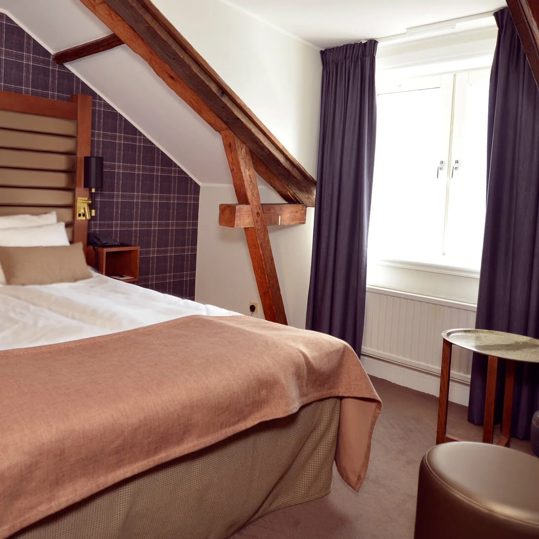 A neatly made double bed in a cozy room with exposed wooden beams and tartan patterns on the walls.