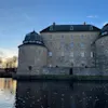Örebro slott, ett storslaget stenslott med runda torn, speglat i lugnt vatten under en delvis molnig skymningshimmel.