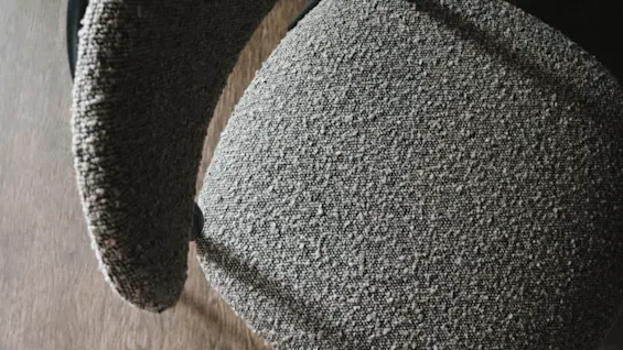 Gray upholstered chair, viewed from above, showing a curved backrest and seat. Positioned on a wooden floor, emphasizing a cozy, modern interior setting.