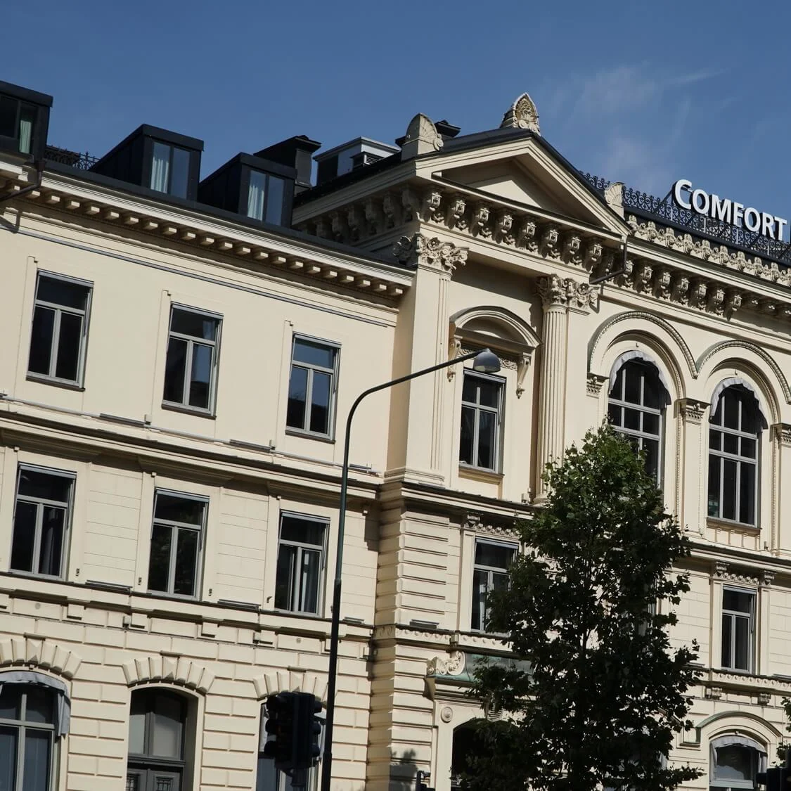Classic facade of 'Comfort Hotel Malmö' with arched windows and a glass rooftop, against a clear sky.