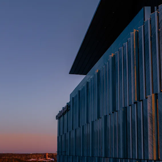 Clarion Hotel Helsinki Airportin julkisivu, joka esittelee modernia muotoilua ja teksturoituja paneeleja, jotka heijastavat auringonlaskun lämpimiä sävyjä.