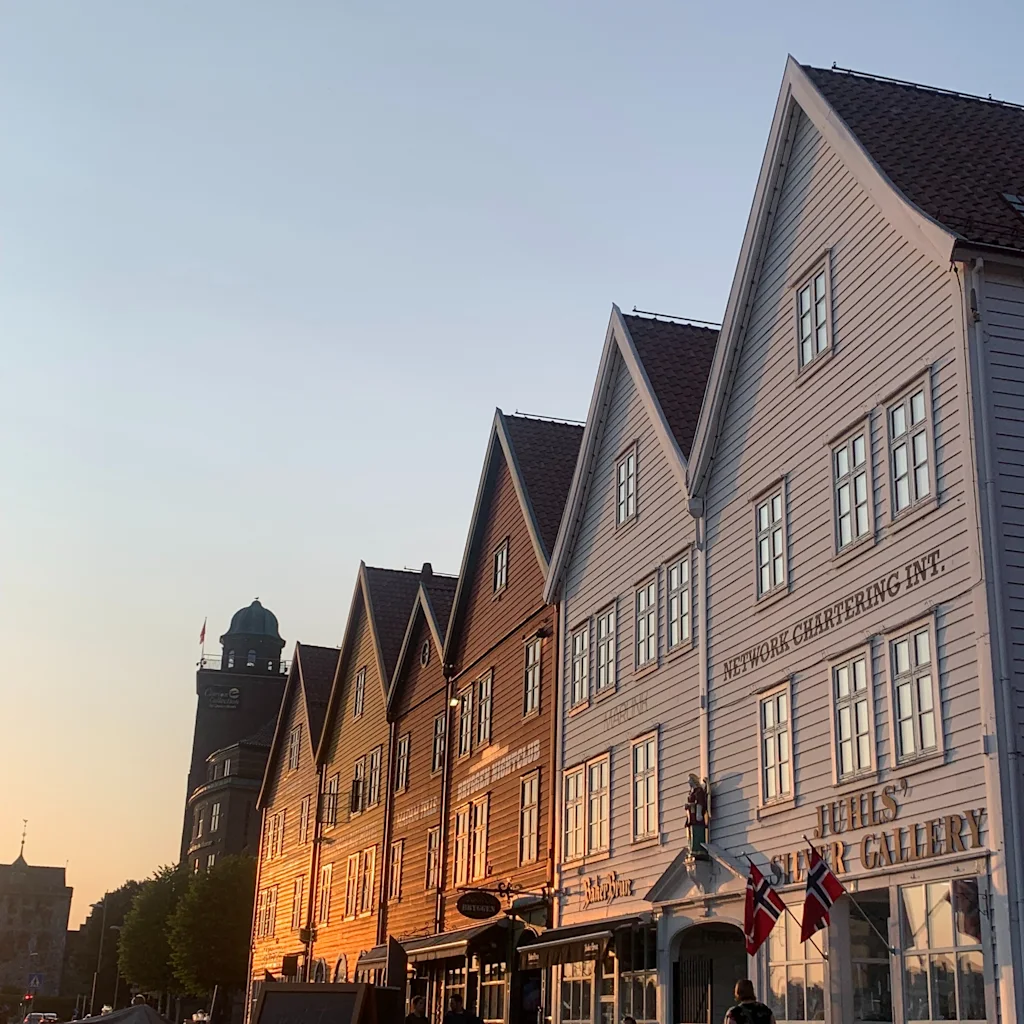 Bryggen Bergenissä, Norjassa, auringonlaskussa. Historiallisia puurakennuksia ja ihmisiä.