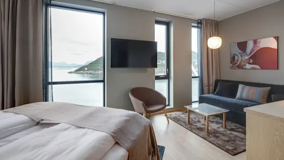 Et hyggeligt hotelværelse med seng, stol og sofa. Et stort vindue tilbyder en smuk udsigt over vandet. Minimal dekoration inklusive et tv og vægkunst forbedrer komforten.