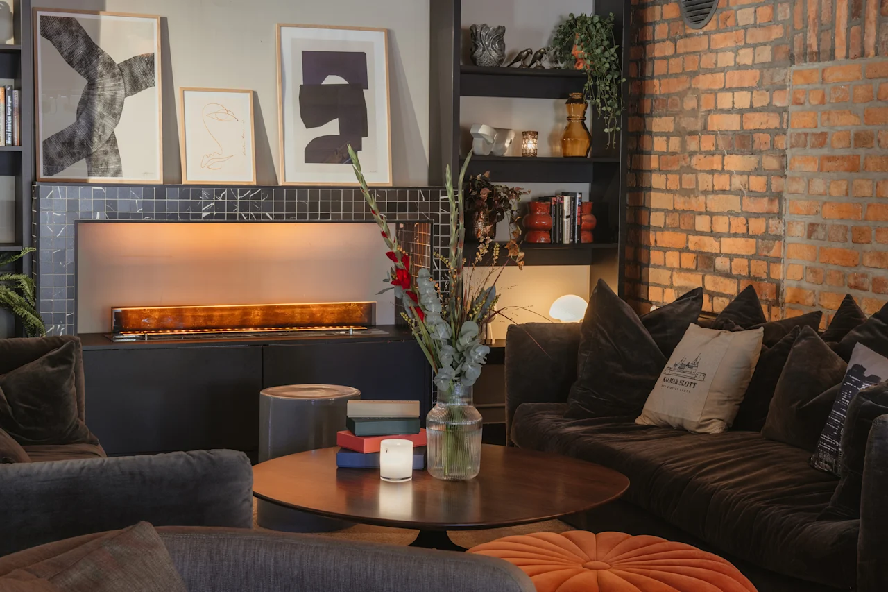 A cozy and stylish lounge area featuring a modern fireplace, plush seating, and a coffee table adorned with flowers and books.