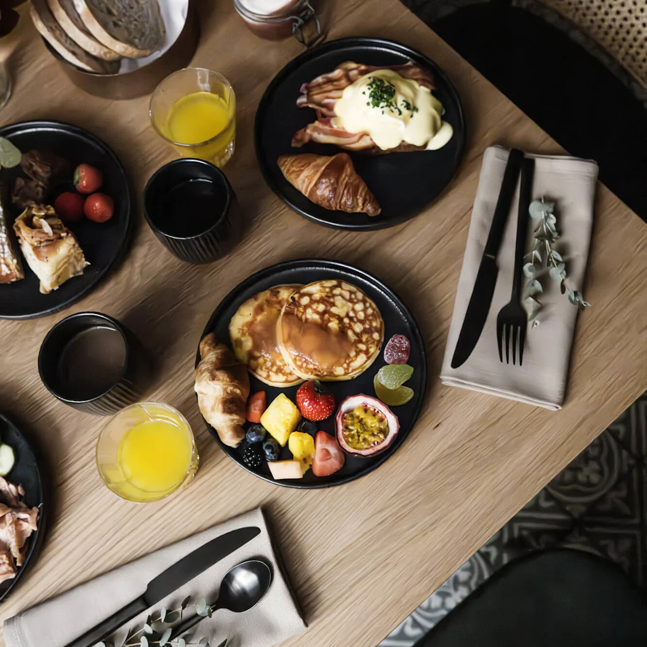 Et udvalg af morgenmadsmad arrangeret på et træbord, antyder et fælles eller buffet-stil måltid.