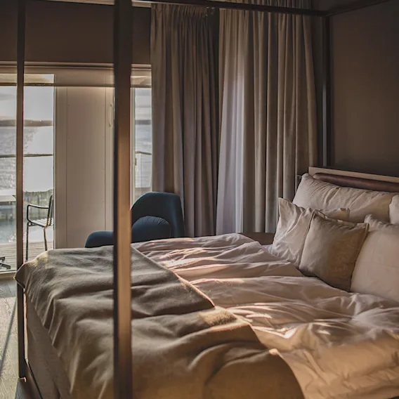 Mysigt hotellrum med en himmelssäng och utsikt över vattnet genom fönstret.