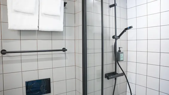 Dusch med skjutglassdörr står oanvänd; två vikta vita handdukar hänger på en närliggande stång i ett kaklat badrum.