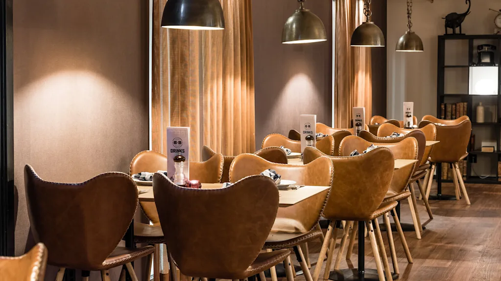 A cozy restaurant interior with pendant lights illuminating a row of leather chairs at wooden tables.