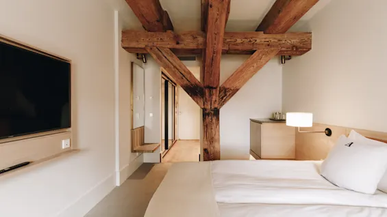 Ett mysigt hotellrum med en bekväm säng, en väggmonterad TV och rustika träbjälkar som ger karaktär åt rummet.