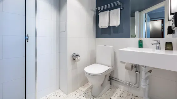 A modern bathroom with a white toilet and sink, two towels hanging, and a glass shower door.