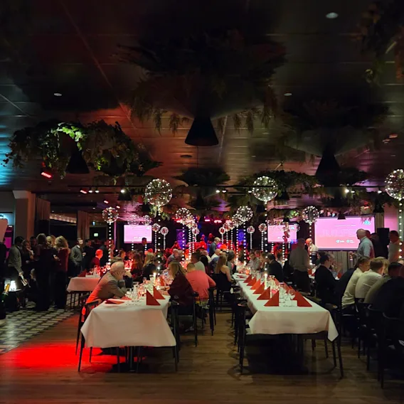 En stor festsal fylld med gäster som sitter vid långbord under en julfest.